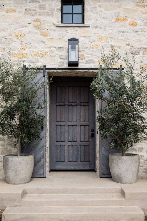 Stunning home exterior with stone entrance, wood door, black lantern lighting and olive trees