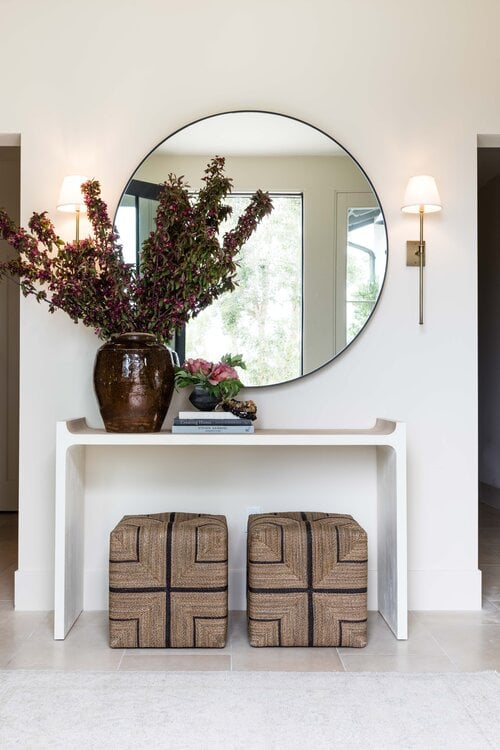 Beautiful modern entryway with console table, round mirror and woven poufs