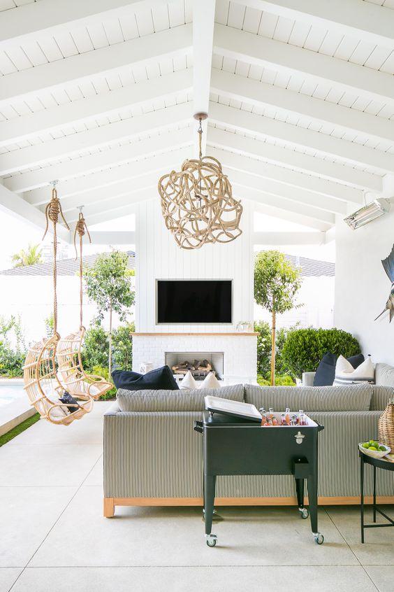 Love this beautiful outdoor living space with hanging swing chairs, an outdoor fireplace, large seating area, and unique woven pendant light - outdoor ideas - covered patio - covered porch - backyard seating - skout interior design