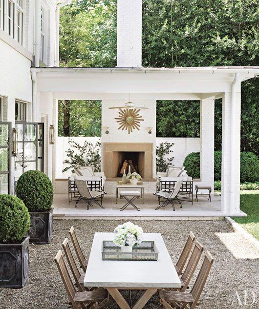 Fabulous outdoor living space with covered patio, gravel dining area, fireplace and ornate wood planters with boxwood topiaries - outdoor ideas - outdoor oasis - outdoor dining - backyard - Suzanne Kasler - Arch Digest 