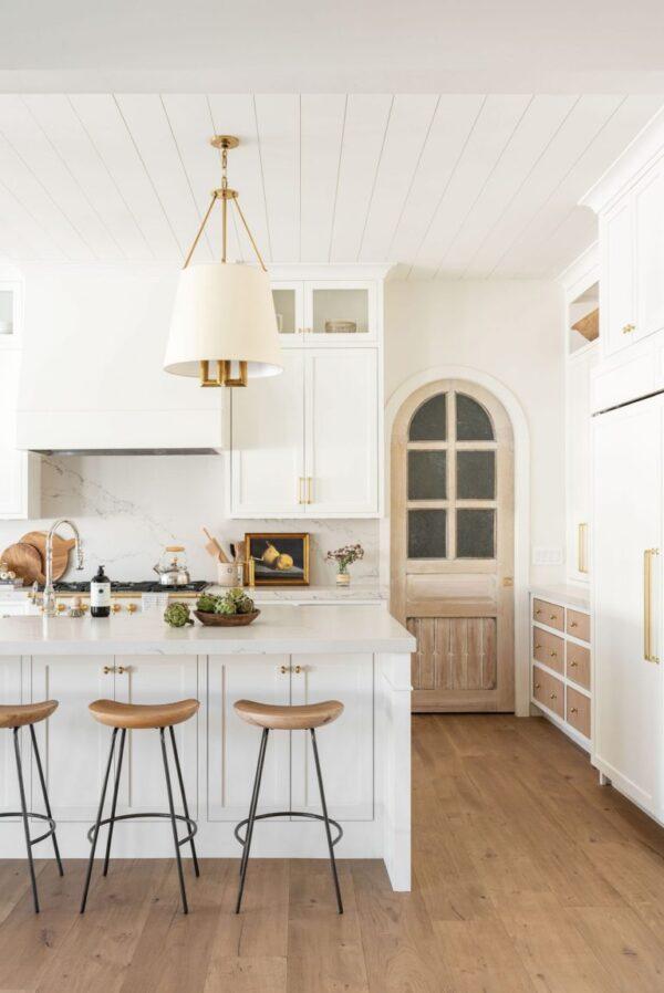 Love this beautiful timeless kitchen design with white cabinets, mixed with the light wood flooring, white oak pantry door and more. The lights over the island are stunning! kitchen remodel - kitchen ideas - kitchen decor - white oak and white kitchen - studio mcgee