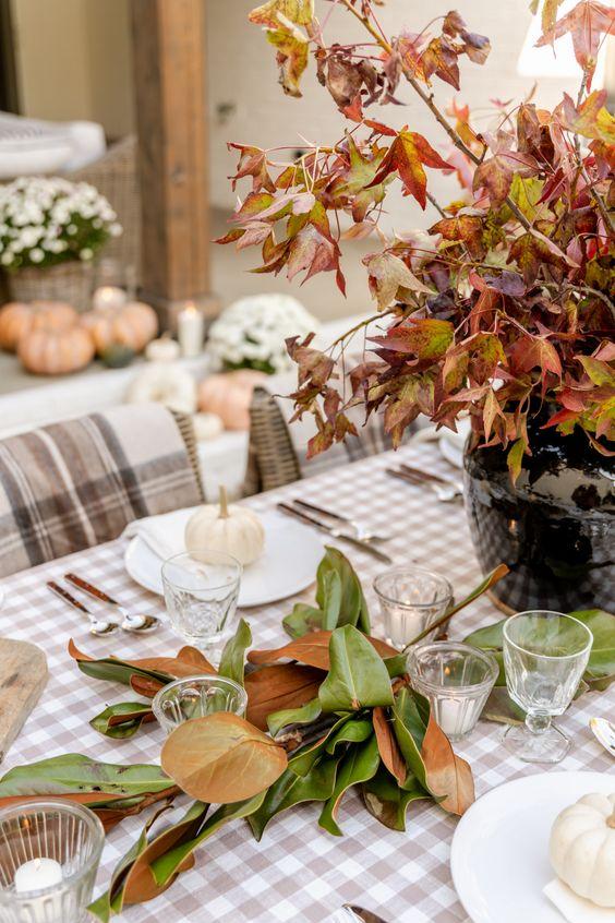 Festive fall branches, foliage, and tiny white pumpkins create a stunning Friendsgiving centerpiece inspired by nature.  From Manor Designs