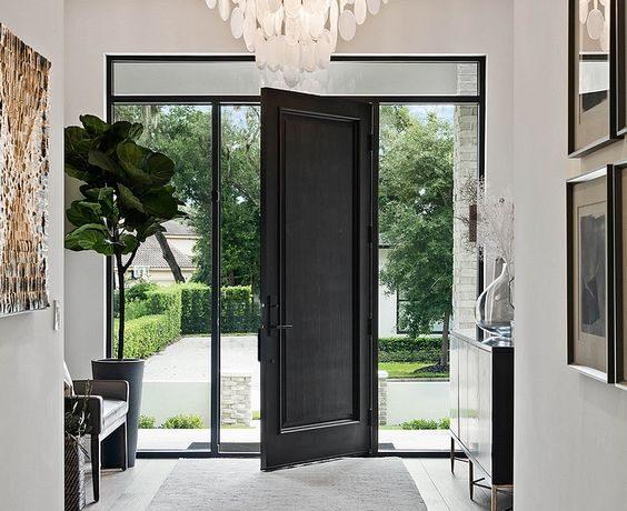 Beautiful modern entryway with a credenza, tiered chandelier, and black front door - m lahr homes