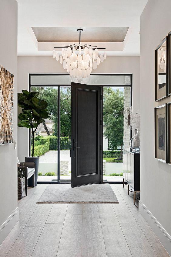 Beautiful modern entryway with a credenza, tiered chandelier, and black front door - m lahr homes
