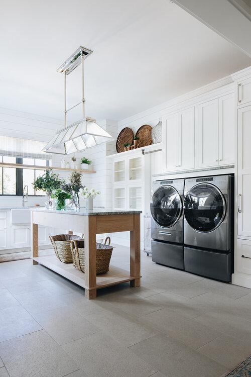 Love this beautiful laundry room with white cabinets and a work table island - kate marker interiors