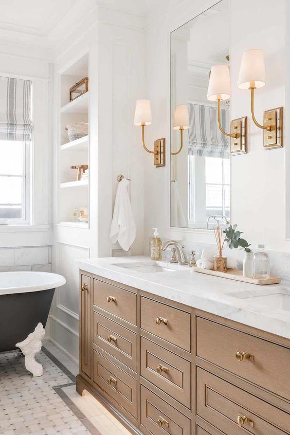Love this timeless bathroom design featuring a warm wood bathroom vanity, double sinks, brass sconces, and a claw foot tub - jenny martin design coastal prestige homes bathroom